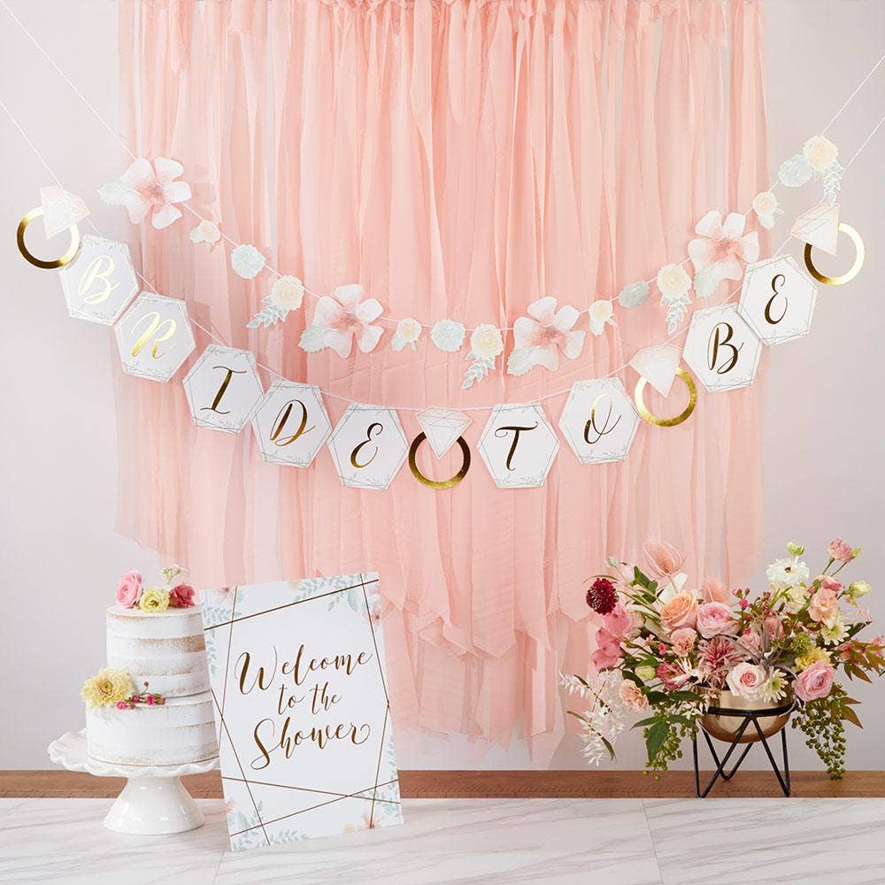 A bridal shower decoration kit displayed, including banners with geometric floral patterns and text, a 'Welcome to the Shower' sign, and a cake with floral decorations.