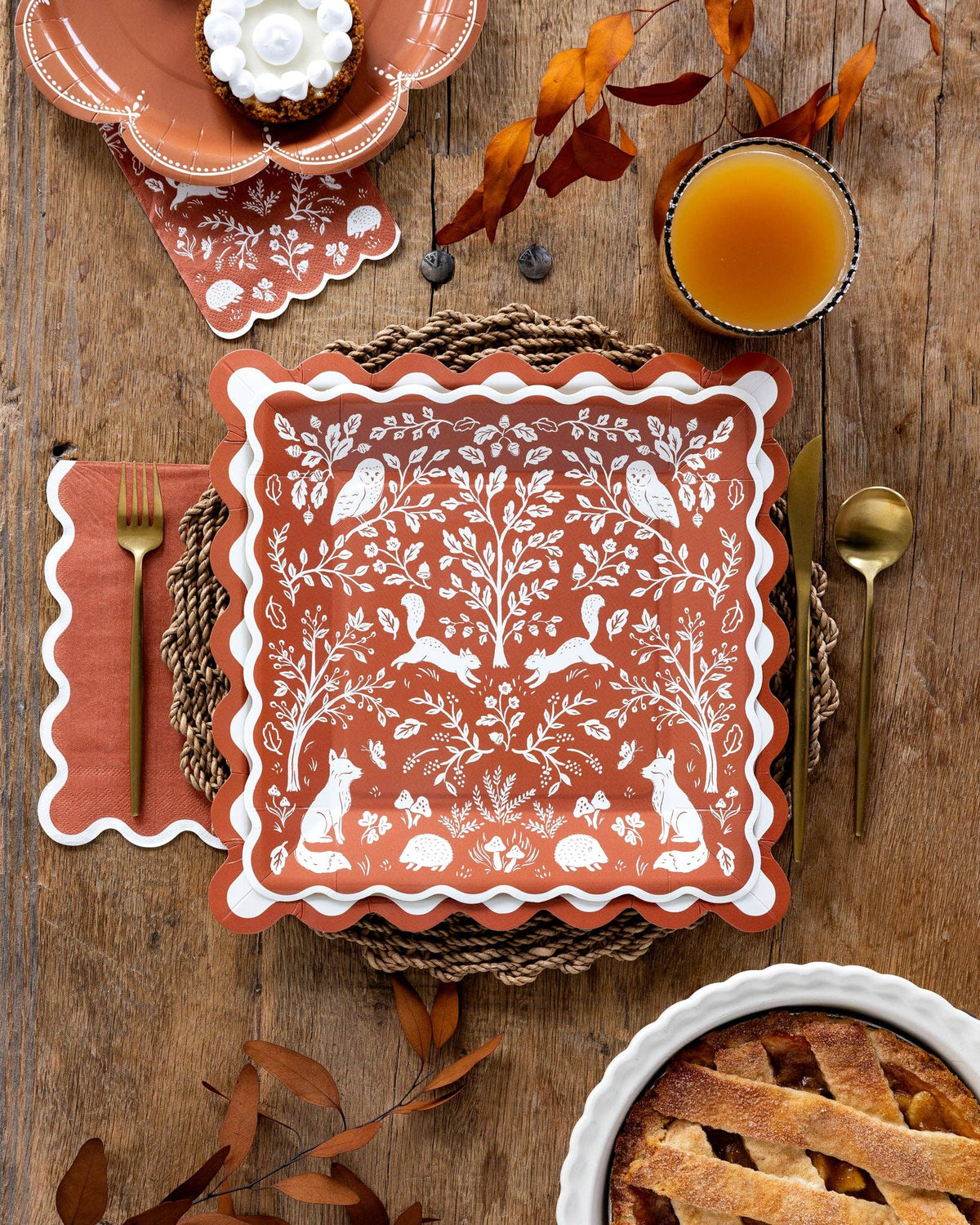 Decorative plate with nature-themed design on a wooden table with autumn leaves and a pie.