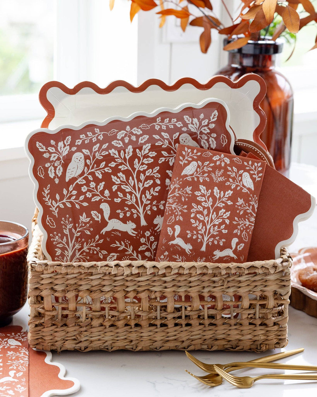 Decorative fall plates with nature-themed design in a wicker basket on a table.