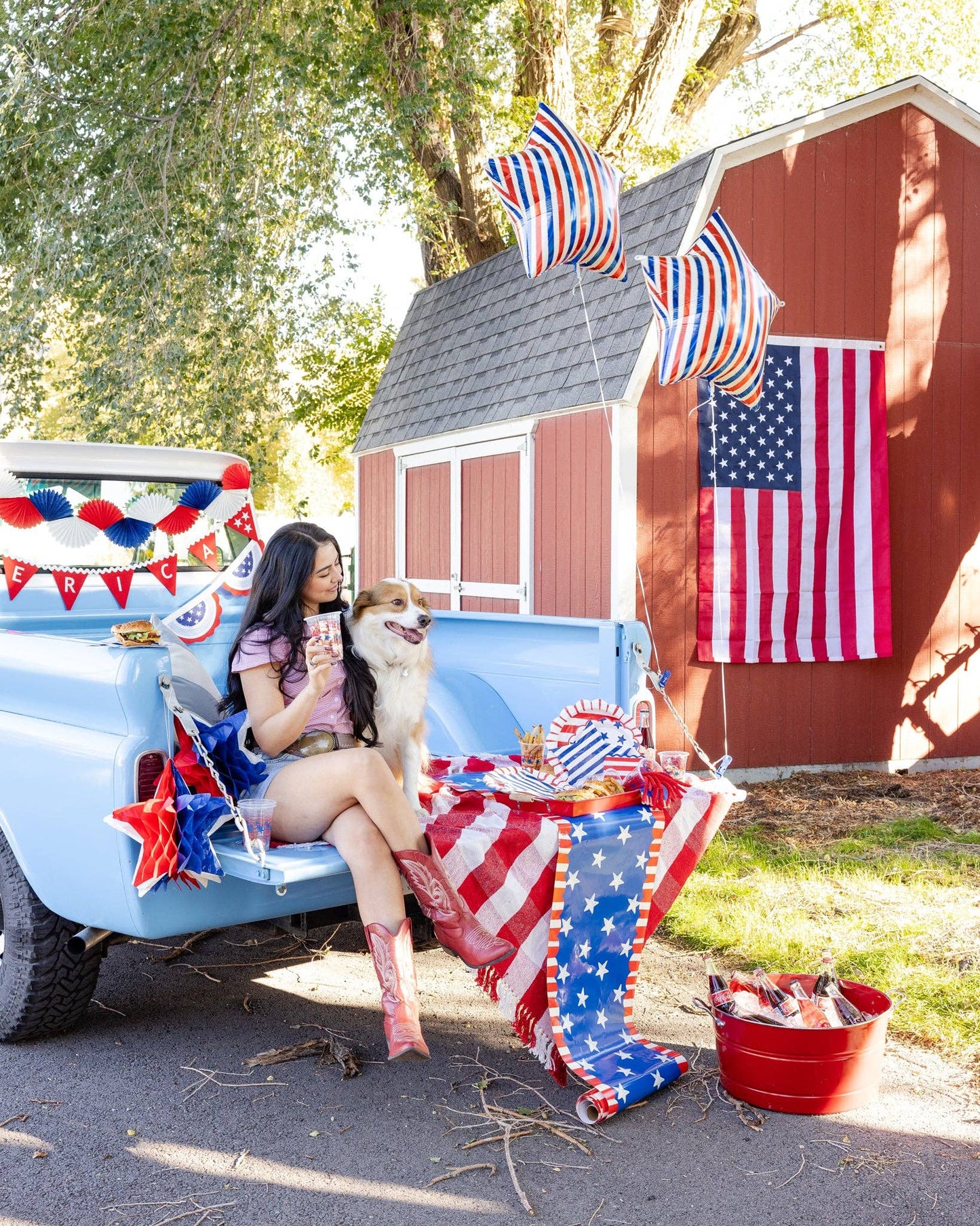 Person sitting in a truck bed decorated with American flags and patriotic decor, with a small building in the background.