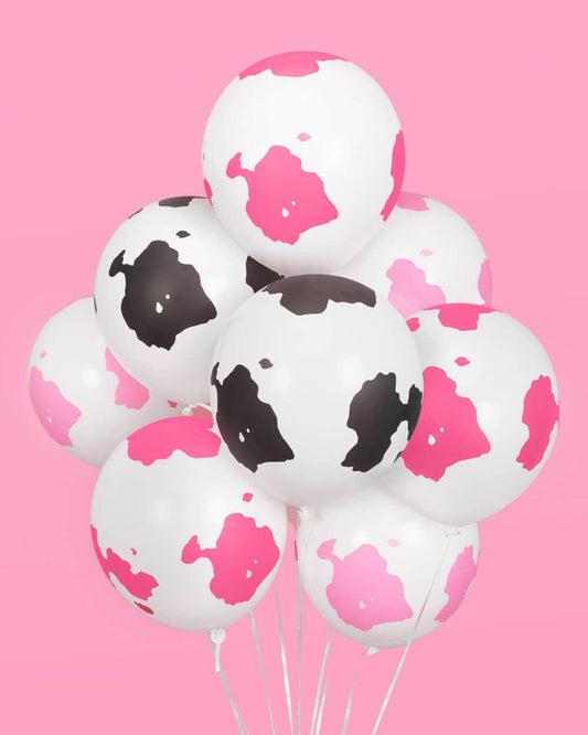 A bouquet of assorted balloons with cow print design on a pink background.
