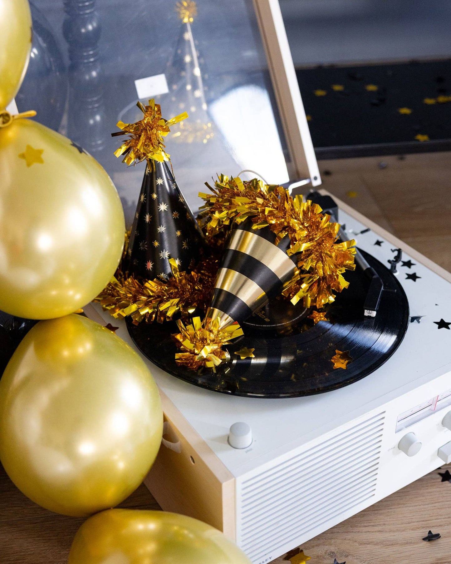 Decorative setup with gold balloons, party hats, and tinsel on a record player.