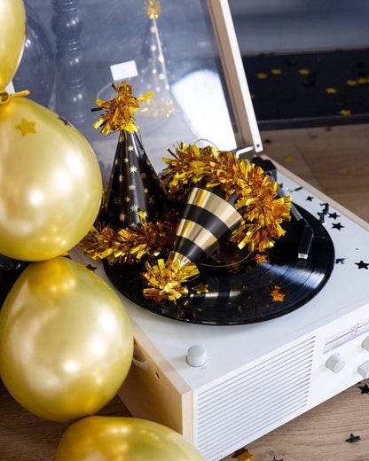 Decorative setup with gold balloons, party hats, and tinsel on a record player.