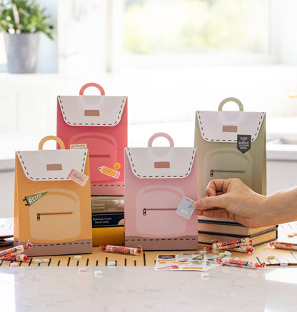 A set of four Back to School themed treat bags in pink, green, yellow, and orange colors, with a decorative sticker sheet, displayed on a table.