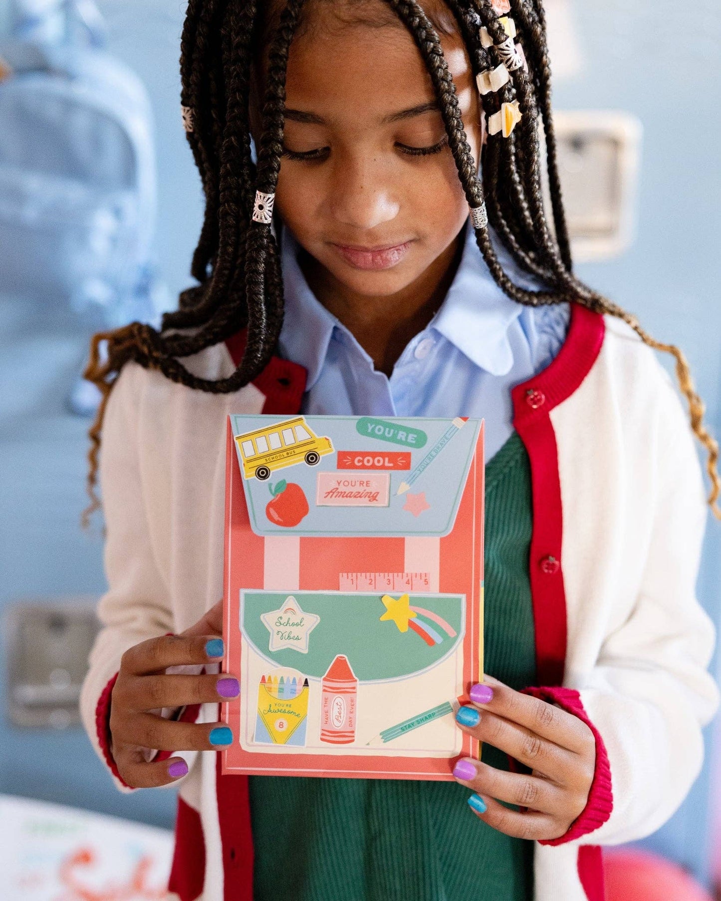 Young girl holding a colorful backpack party favor with stickers in a classroom setting