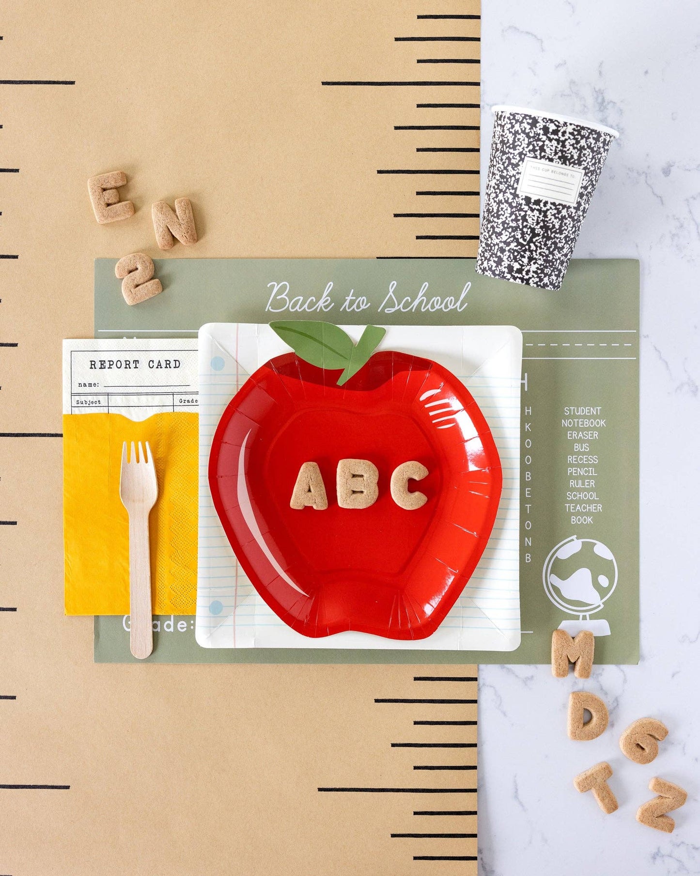 Red apple-shaped plate with 'ABC' letters on a back-to-school themed background with a ruler table runner, notebook plates, and letters.