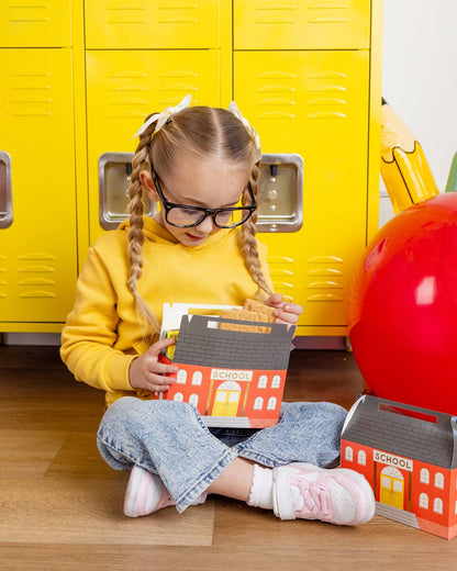 Child sitting on the floor with schoolhouse treat box in front of yellow lockers.