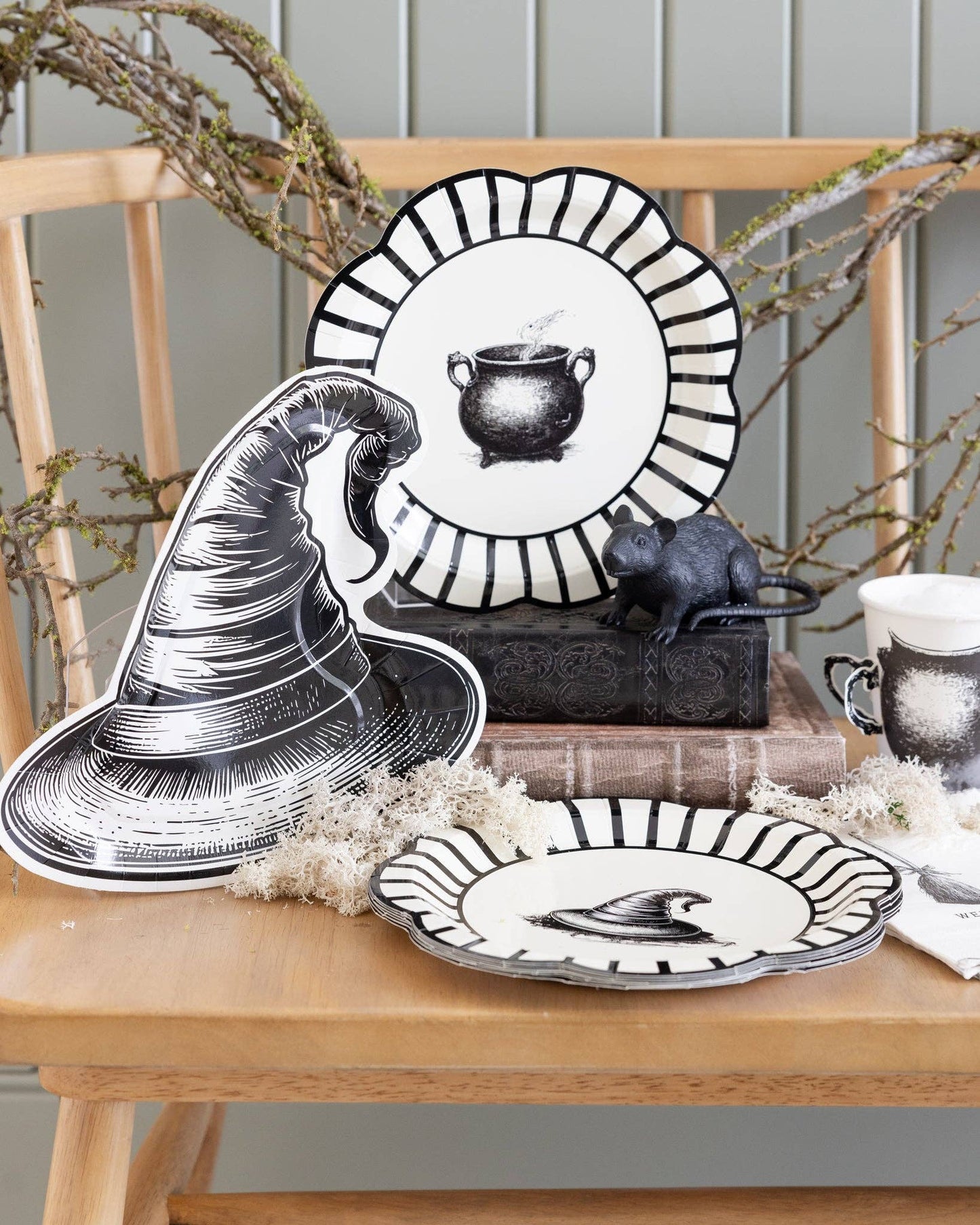 Halloween-themed table setting with decorative plates and cups and a witch hat shaped plate on a wooden bench.