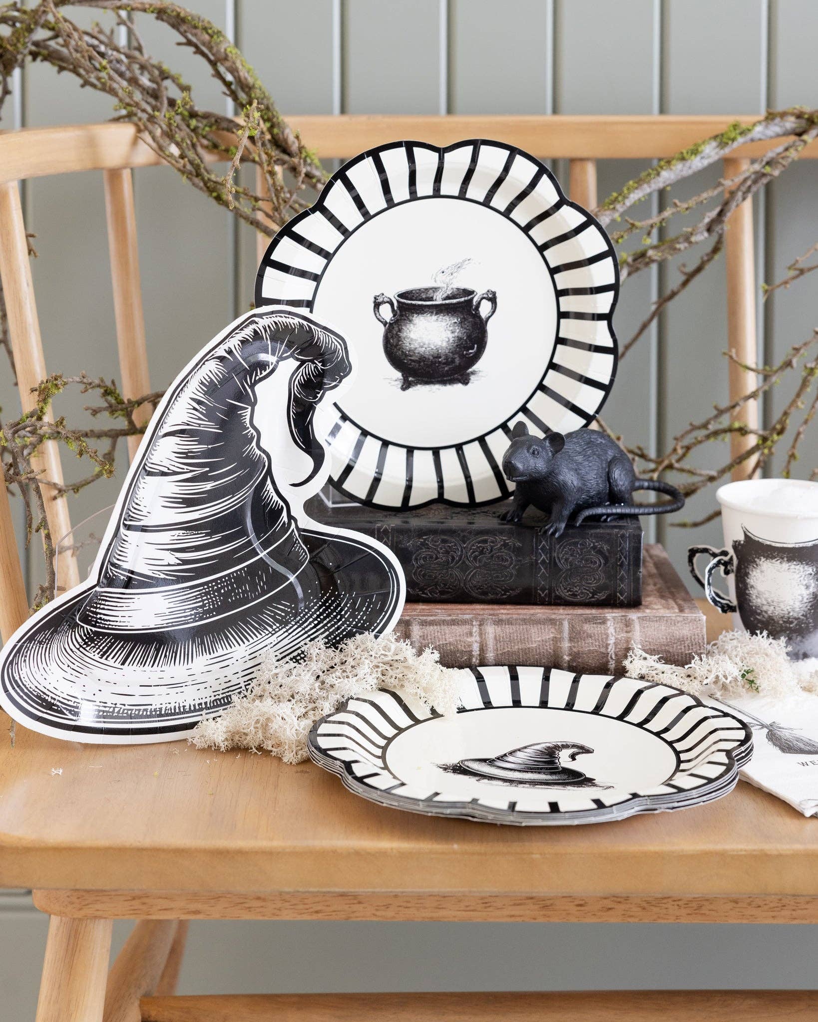 Halloween-themed table setting with decorative plates and cups and a witch hat shaped plate on a wooden bench.