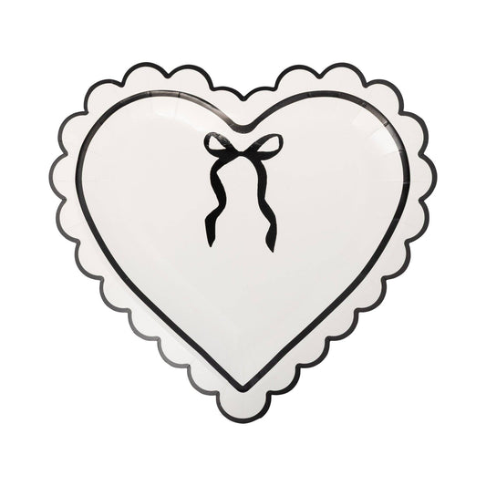 Cream colored heart-shaped paper plate with a black bow design and scalloped edges on a white background.