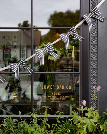 Decorative striped bows on a string in front of a window with 'Flower Bar Co' branding.