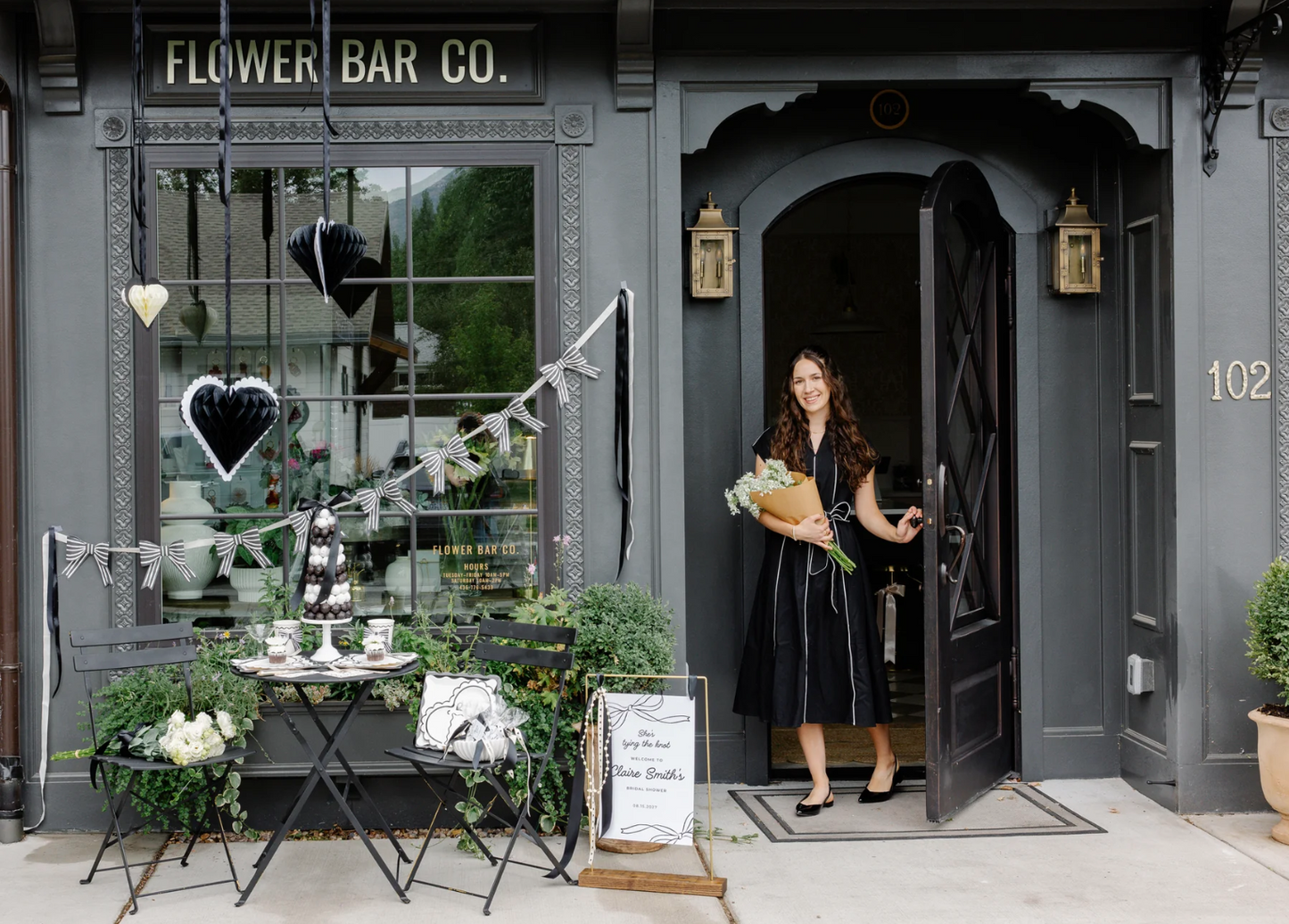 Woman holding flowers exiting a building labeled 'Flower Bar Co' featuring black and white honeycomb heart decorations and coordinating 3D Paper Paper Bow Banner.