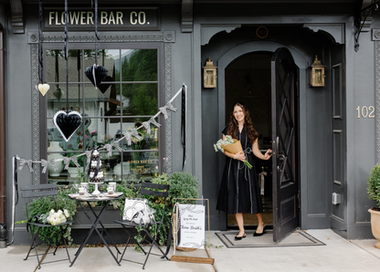 Woman holding flowers exiting a building labeled 'Flower Bar Co' featuring black and white honeycomb heart decorations and coordinating 3D Paper Paper Bow Banner.