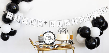 Black and white balloons with 'Happy Birthday' banner and cake on a table.