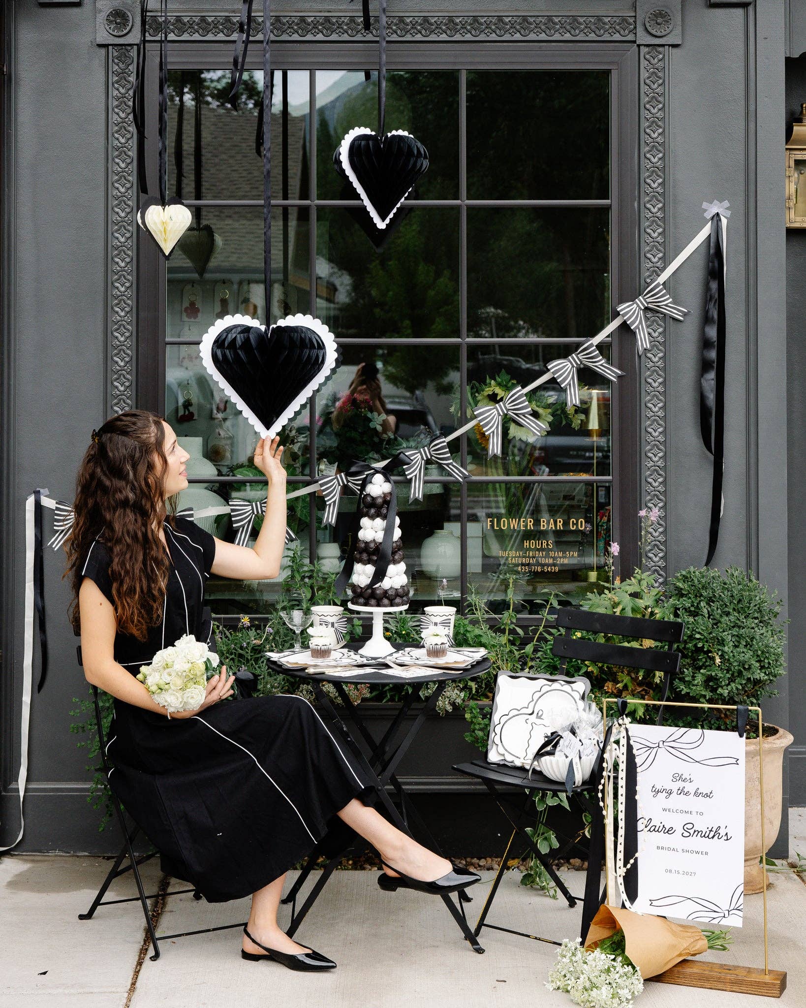 Woman holding a black honeycomb heart-shaped decoration in an outdoor setting with a table and plants.