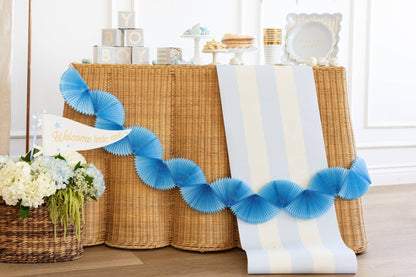 Decorative blue tissue paper accordion-style garland on a brown wicker table with flowers and boy baby shower decor items.