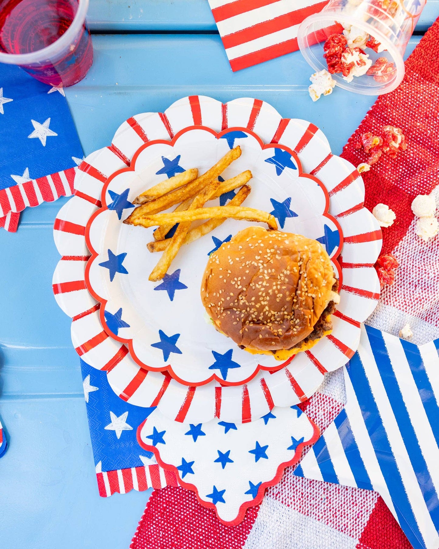 Hamburger with fries on a decorative patriotic plate with star patterns, set against a blue tablecloth.