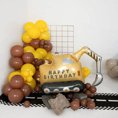Decorative birthday balloon arch with a gold bulldozer-shaped balloon featuring 'Happy Birthday' text, surrounded by yellow and brown balloons on a white background.
