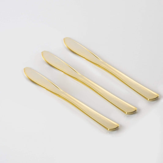 Three gold plastic knives on a light gray background.