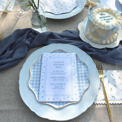 Table setting with a blue and white gingham paper plate, cake, and decorative items.