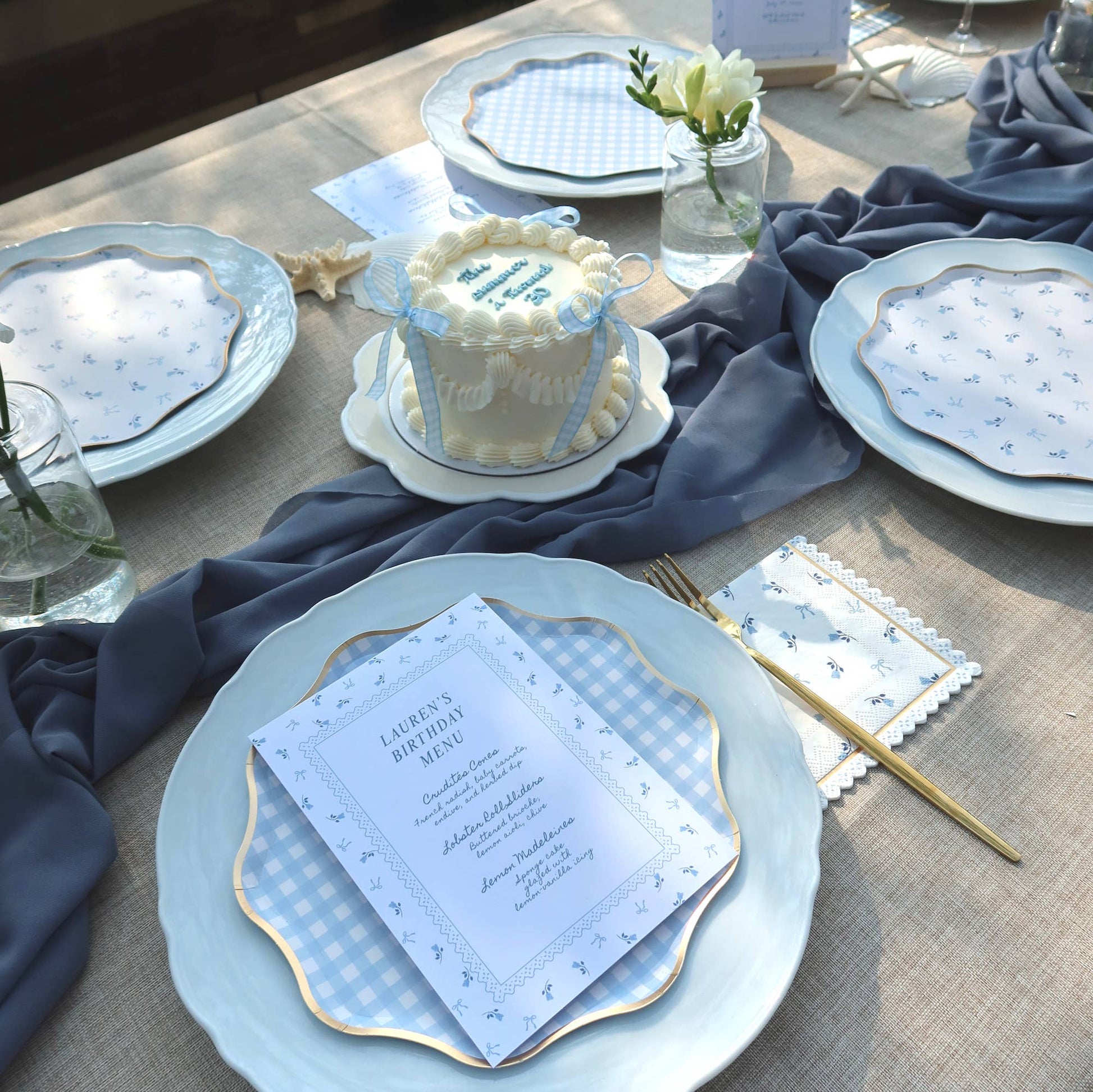 Table setting with blue and white coastal theme, including a cake and place cards.