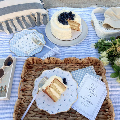 Picnic setup with cake, plates, and flowers on a striped blanket