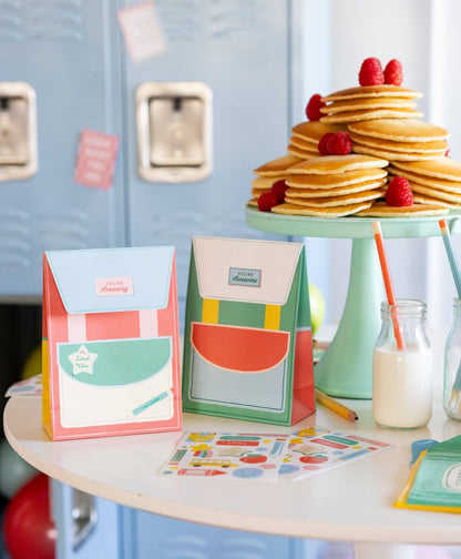 Colorful school-themed backpack favor bags on a table with pancakes and raspberries.