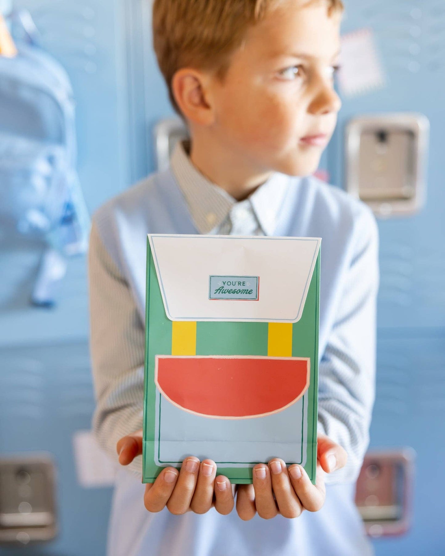 Child holding a colorful party favor in a backpack design against a blue lockers.