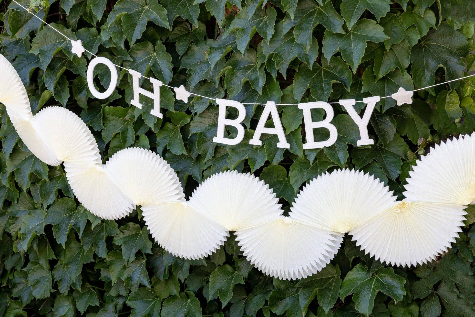 Decorative cream-colored accordion tissue garland against a green leafy background.