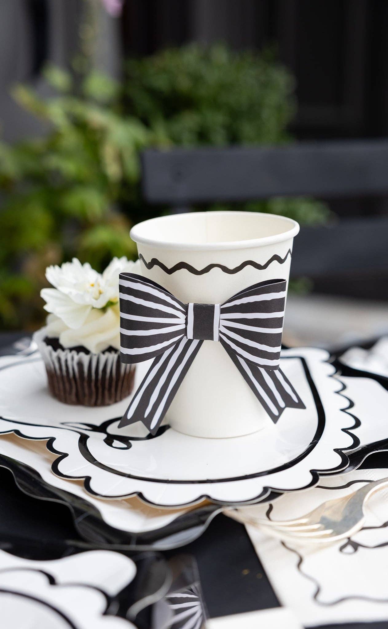 White cup with black bow design on a decorative paper plate with a blurred background.