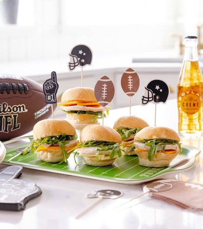 Mini burgers on a platter with football-themed picks, a bottle of cream soda, and a football in the background.