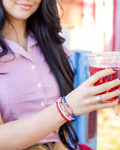 Person holding a red drink with colorful patriotic bracelets on a blurred background