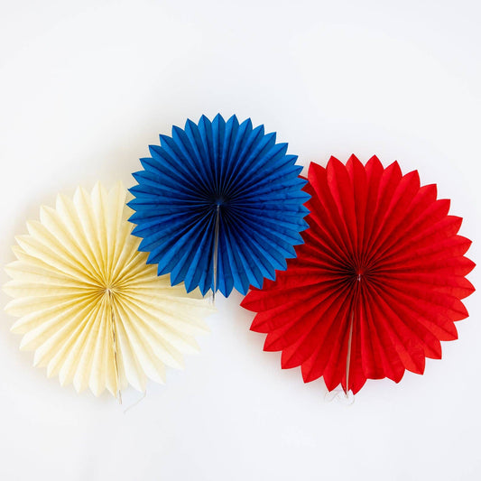 Three paper fans in blue, red, and cream on a white background