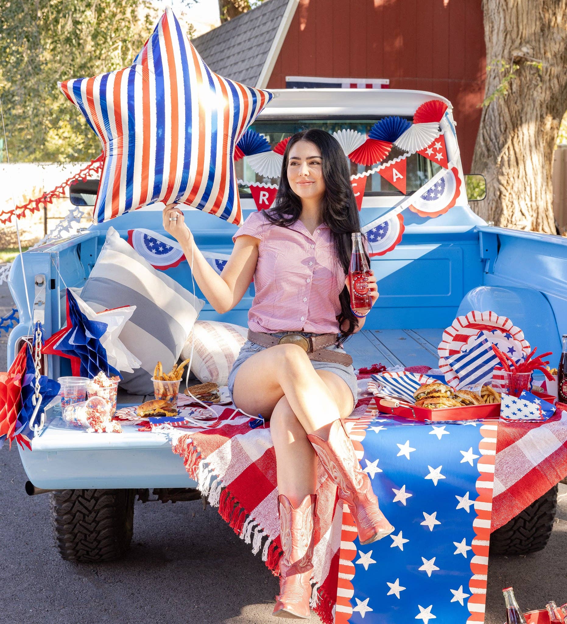 Woman sitting in an Americana decorated truck bed with patriotic decorations and food.
