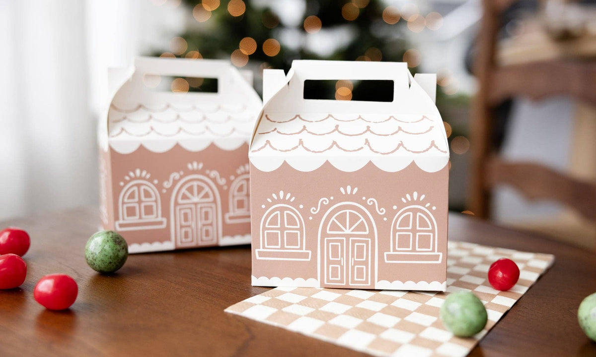 Two decorative treat boxes with gingerbread house design on a table with candy.