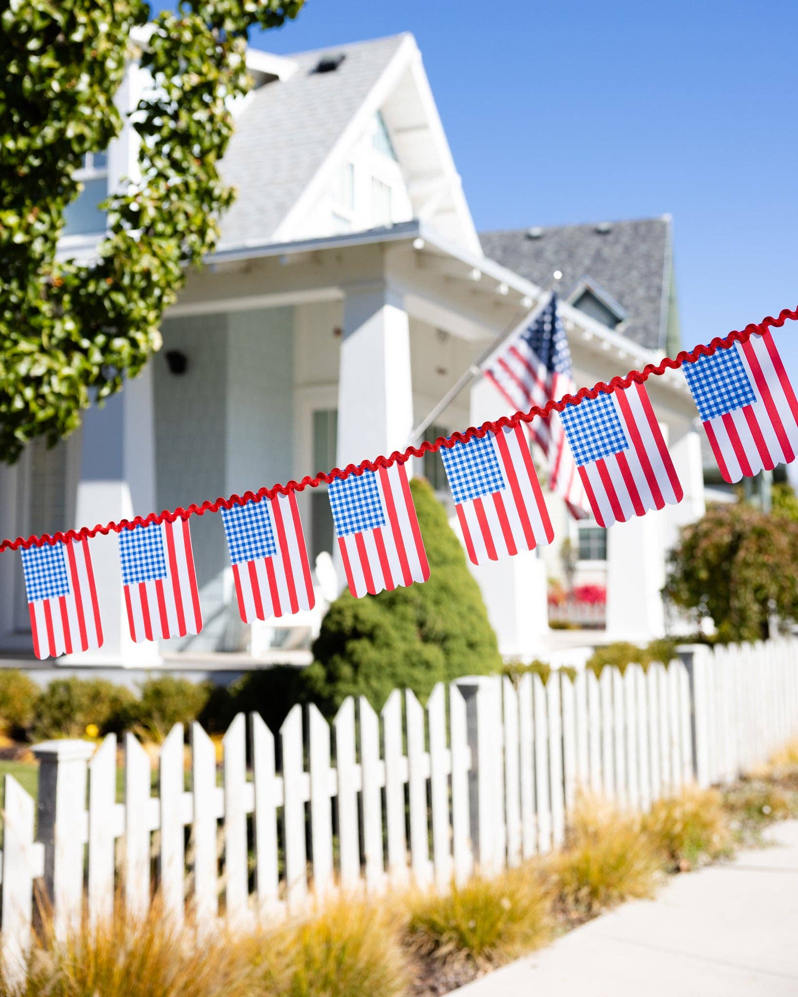 American flag banner in front of a white house with a white picket fence.