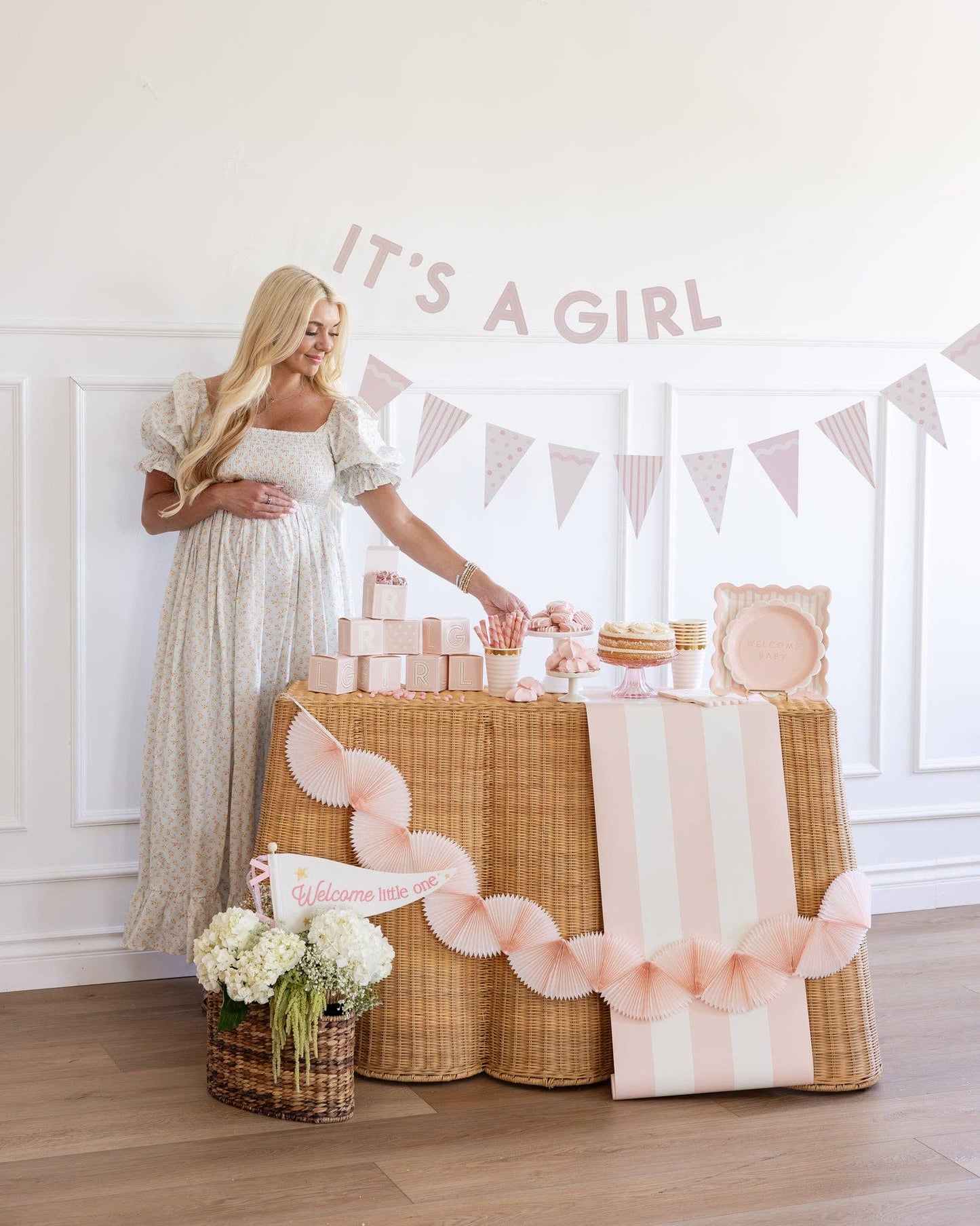 Woman in a long dress standing next to a decorated party table with 'It's a Girl' banner.