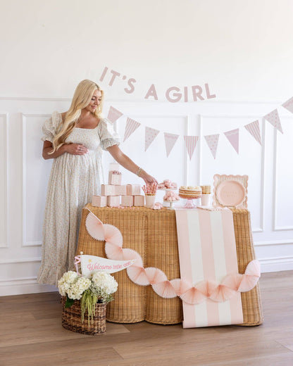 Woman in a long dress standing next to a decorated party table with 'It's a Girl' banner.
