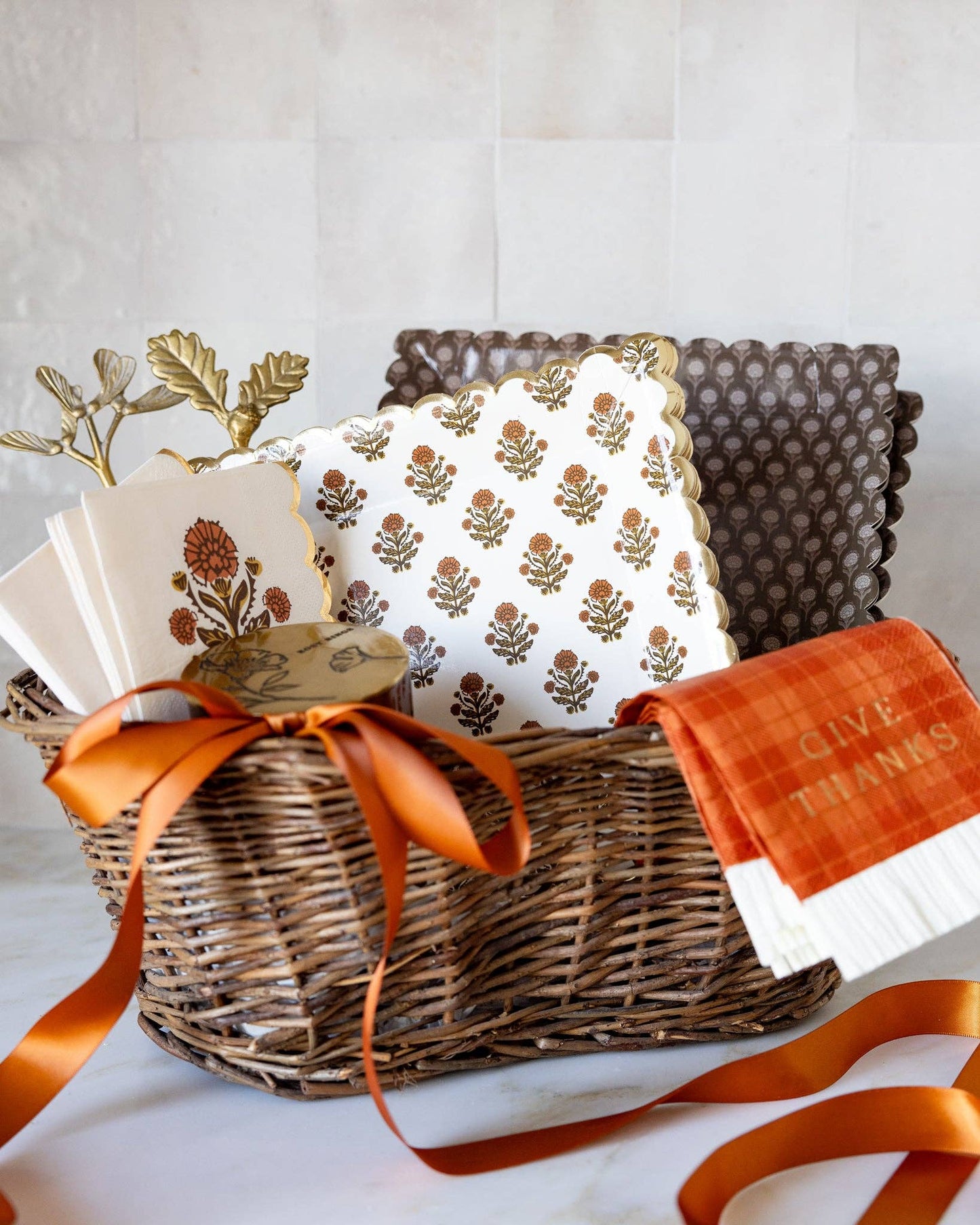 Gift basket with decorative fall tableware items including paper plates, napkins, and ribbons on a light background