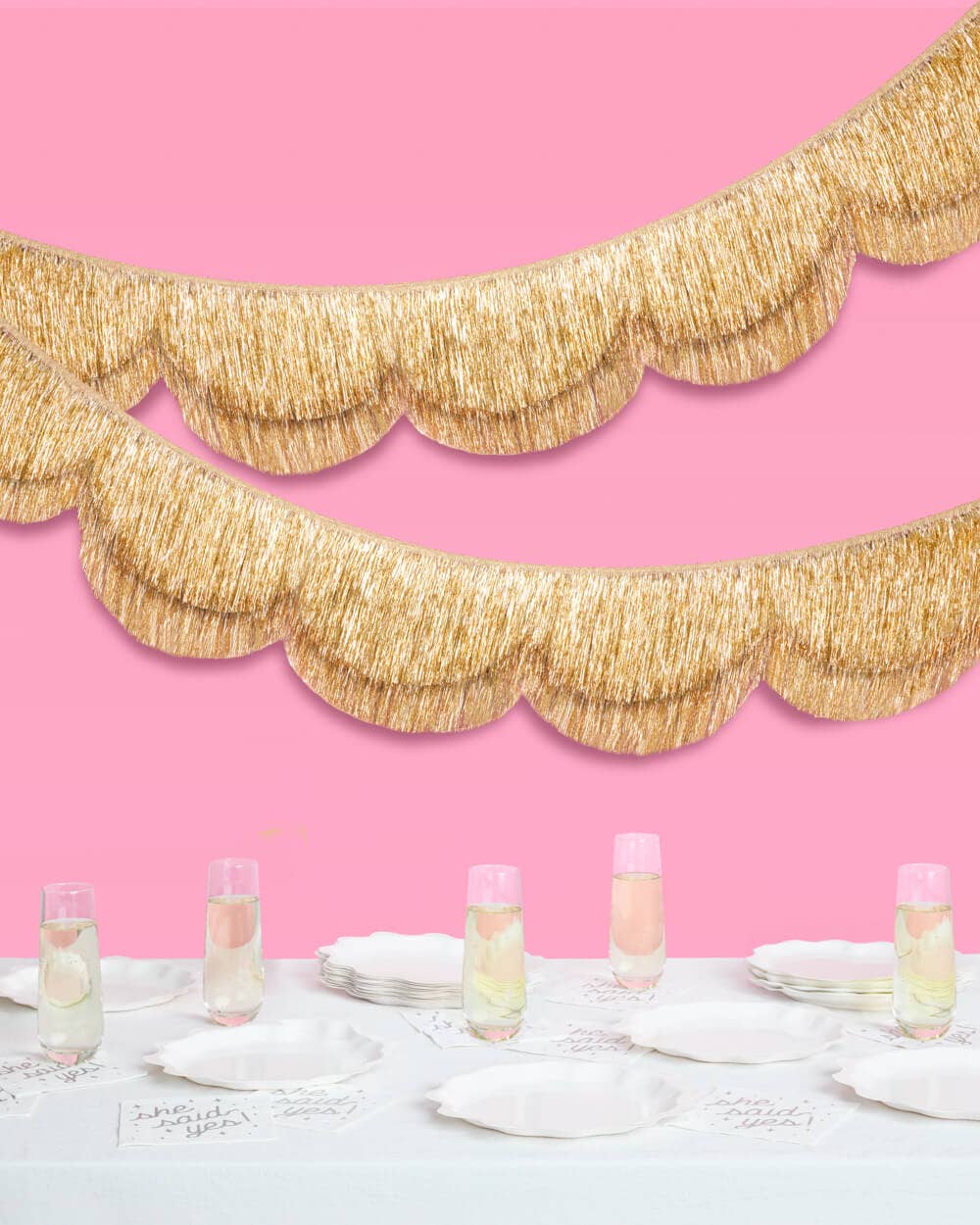 Gold scalloped garland against a pink wall with a table setting.