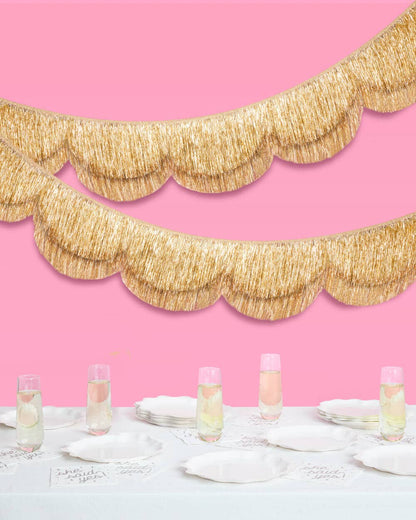 Gold scalloped garland against a pink wall with a table setting.
