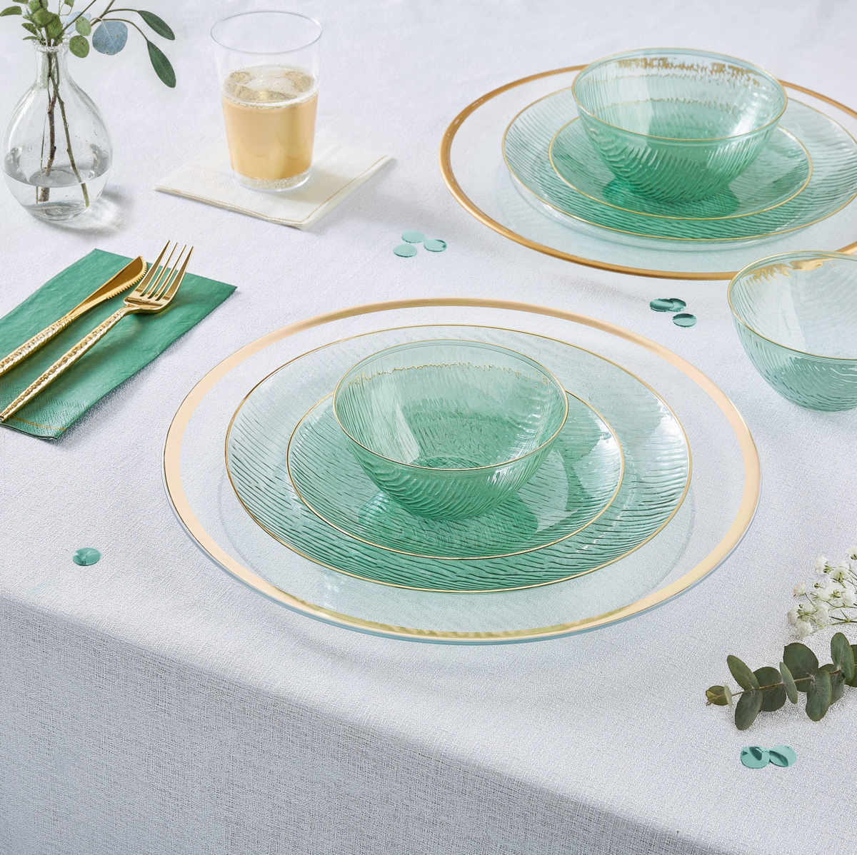 Green glass dinnerware set with gold plastic cutlery on a white tablecloth.