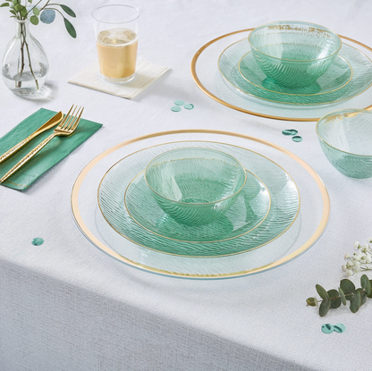 Green glass dinnerware set with gold plastic cutlery on a white tablecloth.