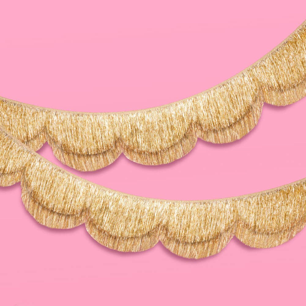 Gold scalloped garland with fringe trim on a pink background.
