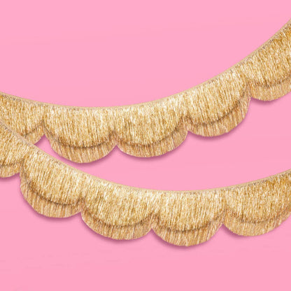 Gold scalloped garland with fringe trim on a pink background.