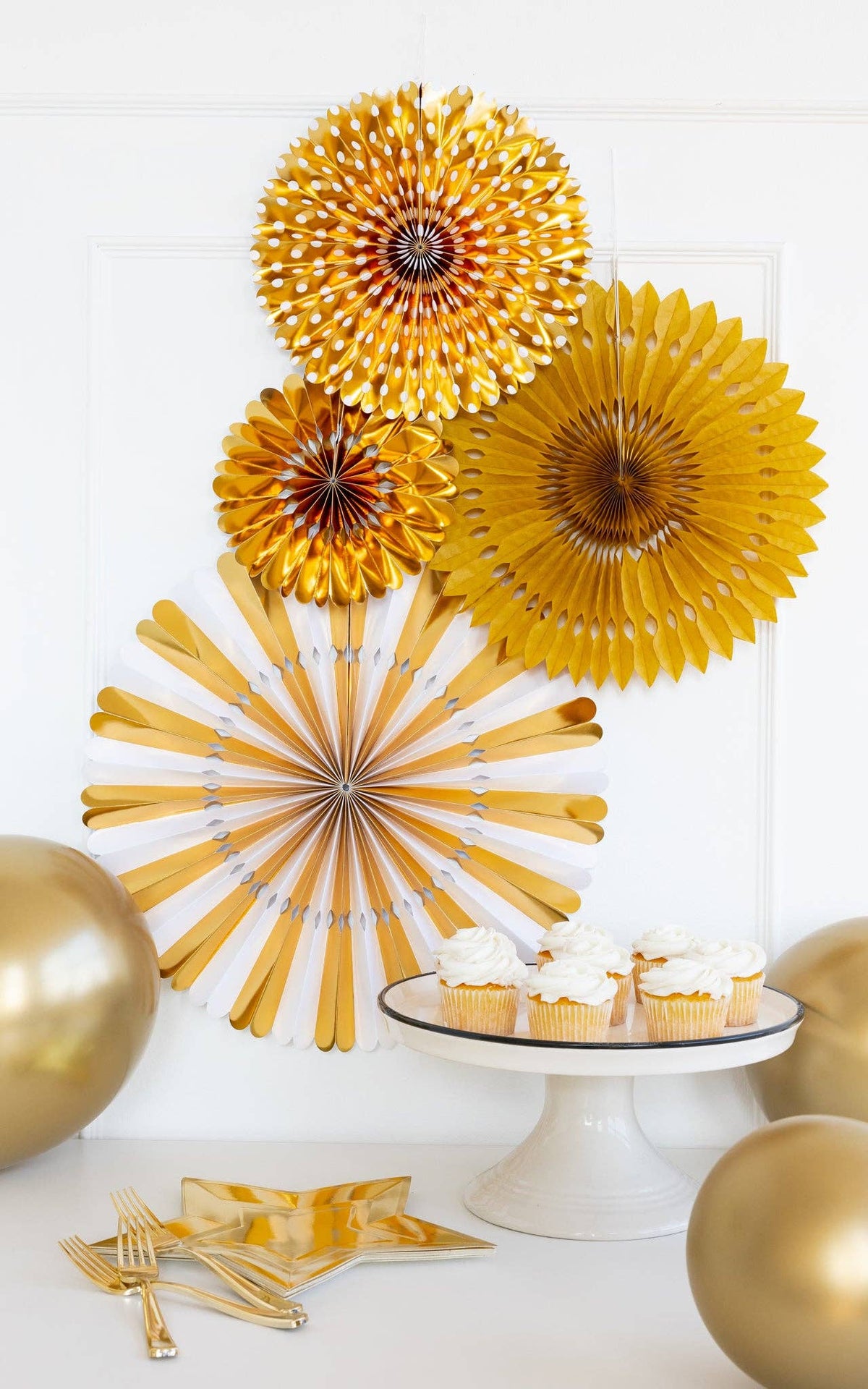 Decorative white and gold paper fans with balloons and a cake stand on a white background.