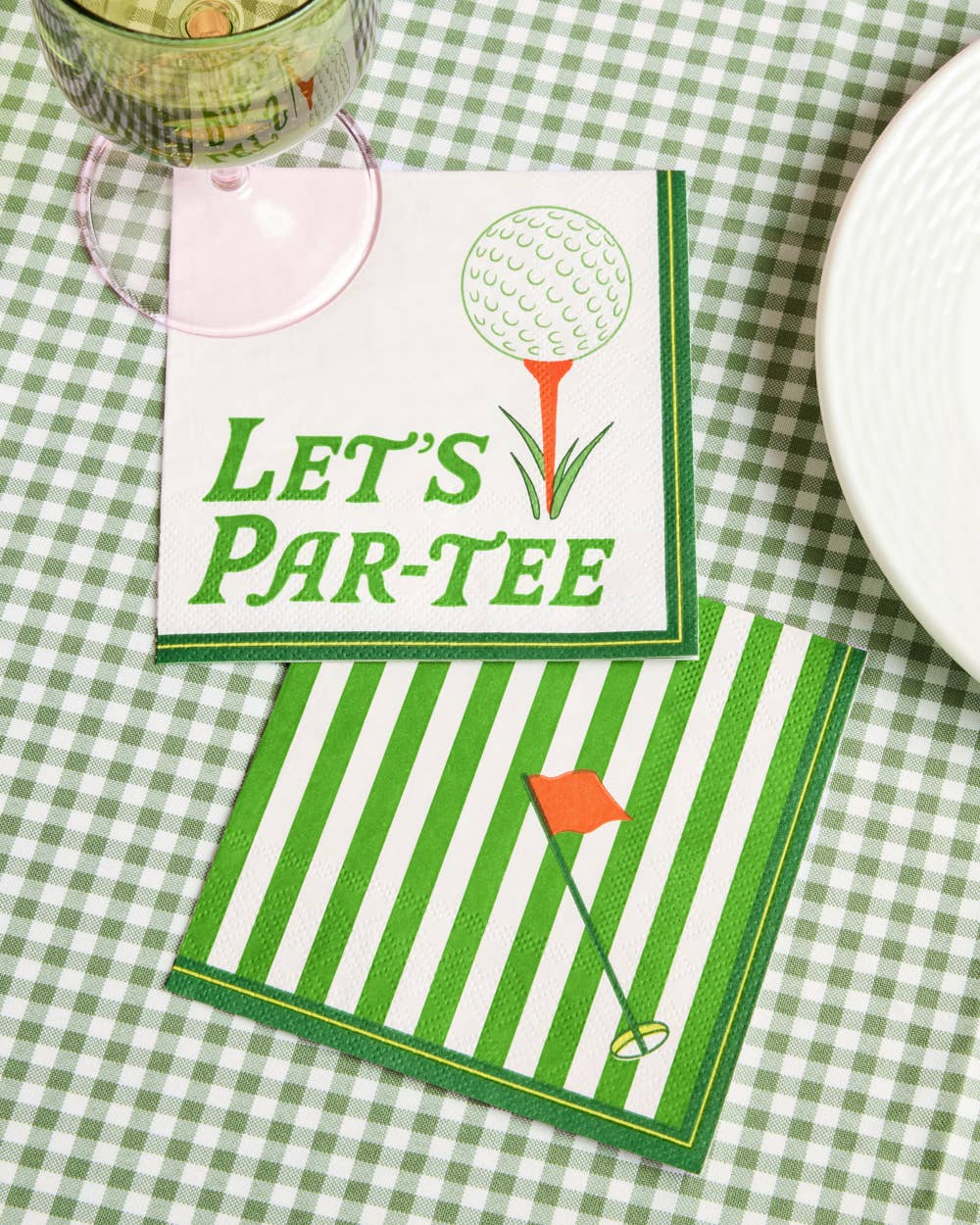 Two napkins with golf-themed designs on a green checkered tablecloth.