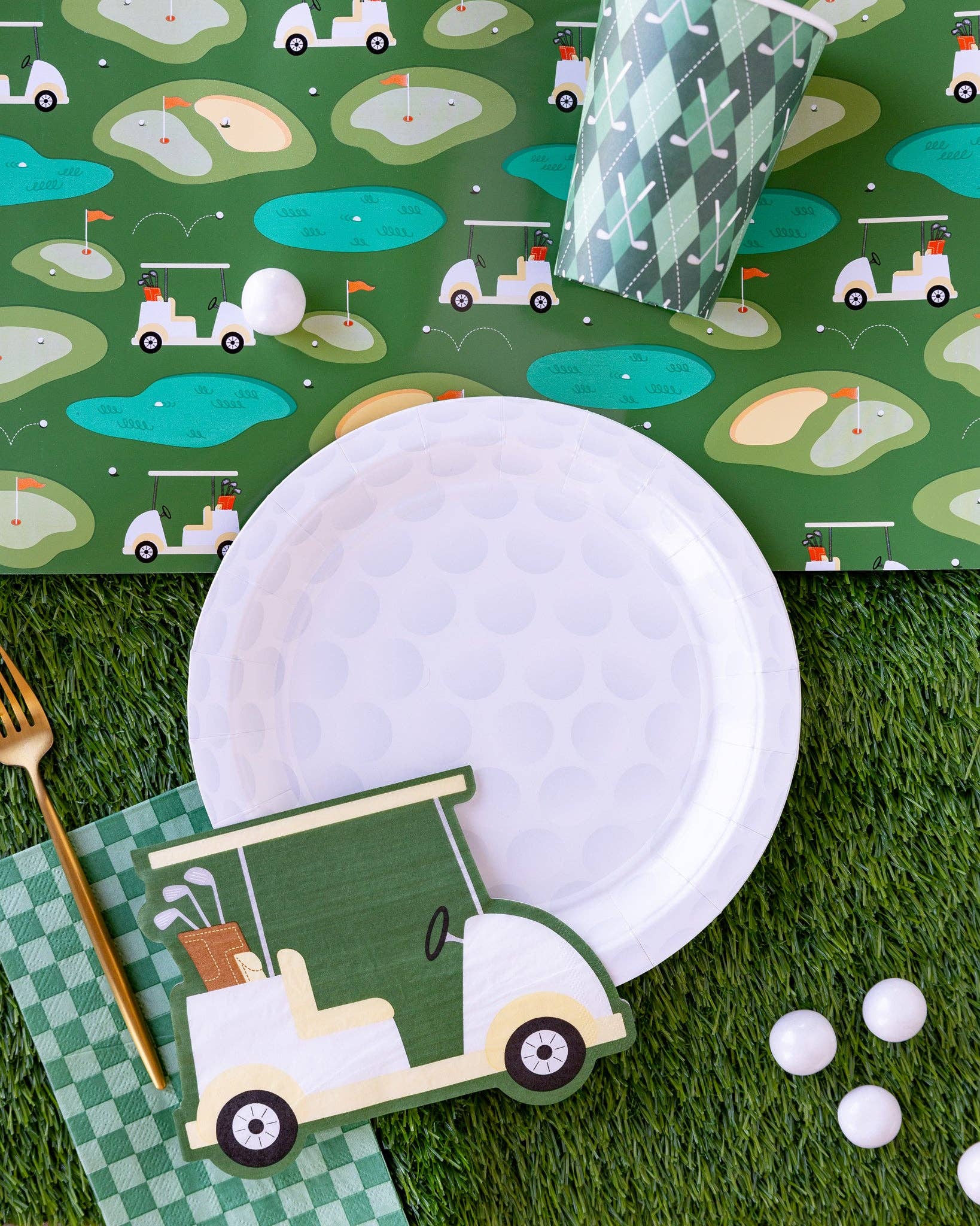 Golf-themed table setting with paper plates, napkins, and cutlery on a green patterned tablecloth.