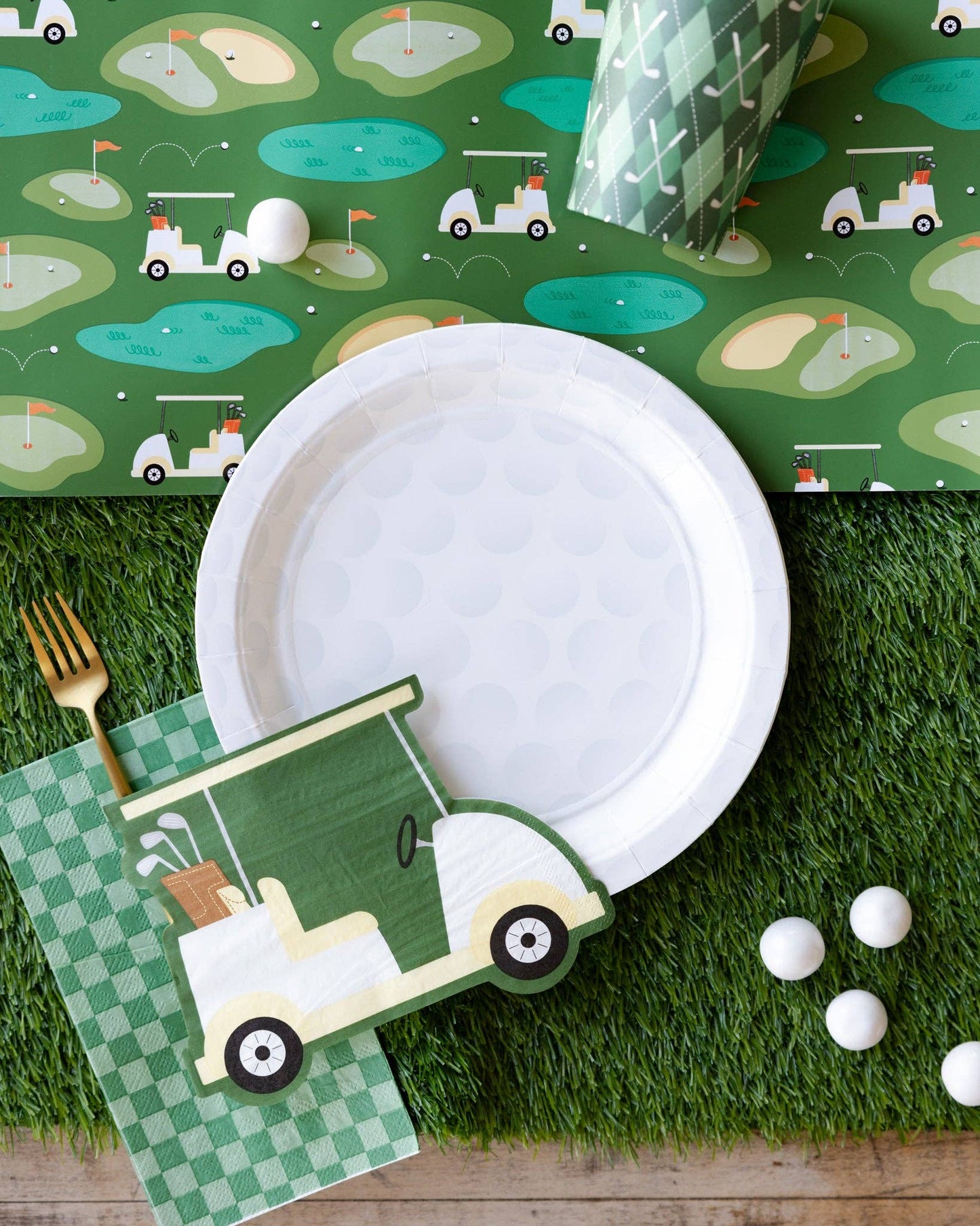 Golf-themed table setting with paper plates, napkins, and golf ball decorations on a green grass-like surface.