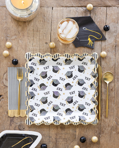 Graduation-themed place setting with napkins and cutlery on a wooden table.